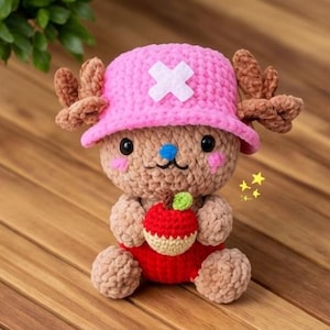 May include: A handmade crochet plush toy of a cartoon character. The toy has a pink hat with a white cross, brown antlers, and holds a red apple. The toy is brown, pink, red, and white. The toy is sitting on a wooden surface.