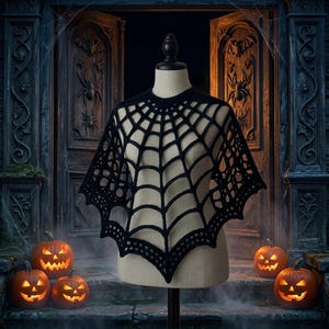 May include: A black crochet poncho featuring a prominent spider web pattern that radiates from the neckline to the scalloped hem. The garment is displayed on a neutral-toned mannequin, showcasing the intricate openwork design of the yarn.