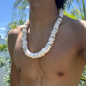 May include: A white shell necklace with a natural, organic design. The necklace is made up of numerous, irregularly shaped white shells strung together. The shells have a slightly rough texture and are strung on a visible cord. The necklace is worn around the neck.