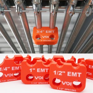 May include: A collection of bright orange plastic conduit spacers featuring white text labels for 3/4 inch, 1 inch, 1 1/4 inch, and 1/2 inch EMT sizes, with specific spacing measurements printed on each unit, including one attached to a metal pipe.