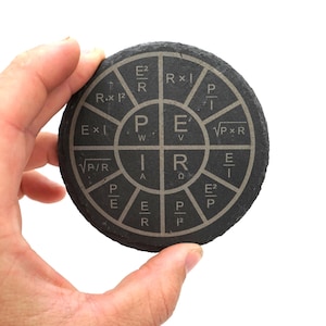 May include: A circular black stone coaster featuring a laser-engraved electrical power wheel diagram. The center displays P, I, R, and E, surrounded by twelve segments containing various electrical formulas such as E squared over R and R times I squared.