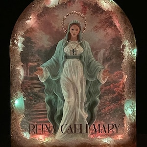Può includere: Un'opera d'arte religiosa raffigurante la Vergine Maria con un'aureola, che indossa un mantello blu e un abito bianco. L'opera è ambientata in una cornice decorativa ad arco con luci e la scritta "REINA CAELI MARY" nella parte inferiore.