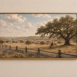 Puede incluir: Una impresión de paisaje enmarcada que muestra un campo amplio de tonos dorados con una valla de madera en primer plano, un árbol grande que da sombra a una vaca longhorn pastando y un horizonte montañoso bajo un cielo con nubes blancas.