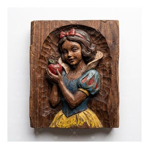 May include: A wooden relief carving of Snow White holding a red apple. The carving is set within a rectangular frame with a carved arch. Snow White wears a blue bodice, yellow skirt, and a red bow.