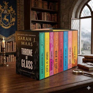 May include: A complete collection of the "Throne of Glass" book series by Sarah J. Maas. The book set features a black box with the series title and author's name, and the individual books have colorful spines. The books are displayed on a wooden surface.