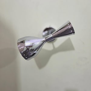 May include: A polished chrome wall sconce featuring a dual-cone design with a central cylindrical connector. The two flared ends are perforated with a series of small, evenly spaced circular holes along the outer edges, creating a reflective finish.