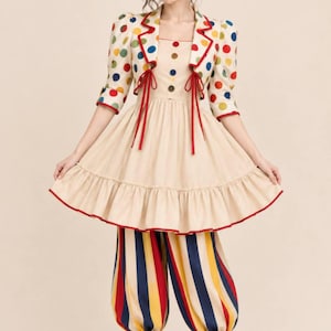 Pode incluir: Um traje de palhaço composto por um vestido bege com bainha franzida e acabamento vermelho, combinado com um casaco curto adornado com bolinhas multicoloridas. O conjunto inclui calças às riscas azuis, amarelas e vermelhas e uma mini cartola.