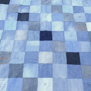 May include: A square patchwork quilt constructed from various shades of blue denim fabric squares. The design features a grid pattern with several integrated denim pockets, some displaying visible stitching details, and a frayed, raw-edge border finish.