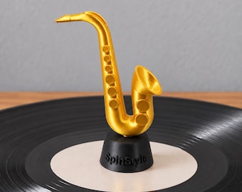 Könnte beinhalten: Eine goldfarbene Saxophon-Figur auf einem schwarzen runden Sockel mit dem eingeprägten Schriftzug SpinStyle auf der Vorderseite. Das Saxophon verfügt über einen gebogenen Hals, einen Schallbecher und mehrere runde Klappen am Korpus, stehend auf einer schwarzen Schallplatte.