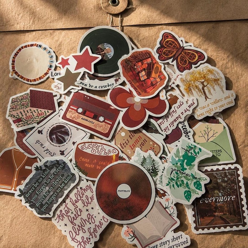 Pode incluir: Uma cole&ccedil;&atilde;o de autocolantes decorativos em v&aacute;rias formas e designs. Os autocolantes apresentam imagens de discos, estrelas, flores, uma fita cassete e texto. A paleta de cores inclui tons de castanho, vermelho e verde.