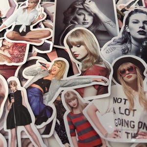 May include: A collection of die-cut vinyl stickers featuring various photographic portraits and performance shots of Taylor Swift. The stickers display diverse outfits, hairstyles, and poses, including one with the text NOT A LOT GOING ON AT THE MOMENT.