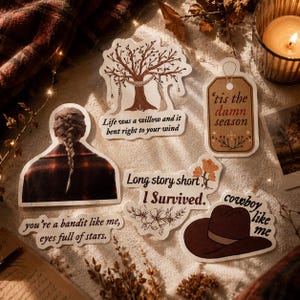 Pode incluir: Uma cole&ccedil;&atilde;o de autocolantes decorativos com v&aacute;rios desenhos e texto. Um autocolante apresenta uma &aacute;rvore com o texto "Life was a willow and it bent right to your wind." Outro diz "'tis the damn season."