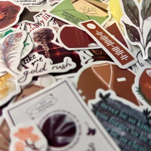 Pode incluir: Uma cole&ccedil;&atilde;o de autocolantes decorativos com v&aacute;rios desenhos e texto. Os autocolantes apresentam ilustra&ccedil;&otilde;es de uma tran&ccedil;a, uma pena e um su&eacute;ter. Alguns autocolantes t&ecirc;m o texto "like me gold rush" e "Writing letters addressed the fire".