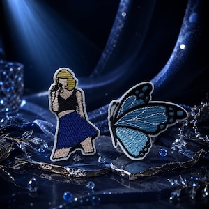May include: Two embroidered patches featuring a figure with blonde hair wearing a black top and blue skirt holding a microphone, and a blue butterfly with black wing edges and white details. The patches are displayed on dark, textured surfaces.