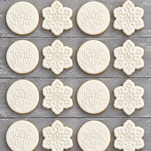 May include: A set of sixteen biscuits arranged in four rows of four, alternating between round biscuits embossed with the text Let it Snow and snowflake-shaped biscuits. Each biscuit features a smooth white icing finish on a light golden brown base.
