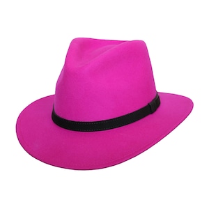 Könnte beinhalten: Ein leuchtend magentafarbener Fedora-Hut mit einem schwarzen Band. Der Hut hat eine klassische Tränenkronenform und eine breite Krempe. Ein modisches Accessoire für jedes Outfit.