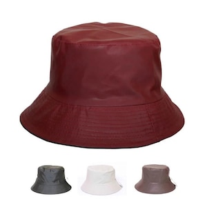 May include: A burgundy bucket hat with a wide brim. The hat is made of a smooth, waterproof material. Below the main hat are three smaller hats in gray, white, and brown.