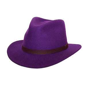 May include: A purple fedora hat with a brown leather band. The hat features a teardrop crown and a wide brim. The hat is made of a soft material. The hat's design is classic.