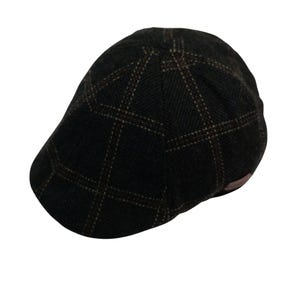 May include: A dark brown flat cap with a plaid pattern. The cap has a classic design, with a rounded crown and a small, stiff brim. The plaid pattern features lines of brown and tan. The cap is made of a textured fabric.