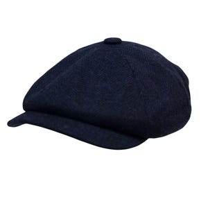 Peut inclure: Casquette gavroche bleu marine avec un motif en chevrons. La casquette a une couronne arrondie et une courte visière rigide. Le tissu a une texture subtile, et la casquette est sur fond blanc.