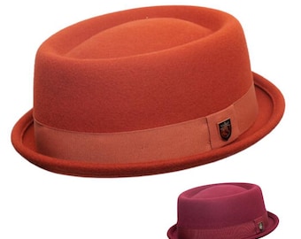 May include: A pork pie hat in a vibrant orange felt material featuring a matching orange grosgrain ribbon band around the crown. A small metallic emblem is attached to the side of the ribbon. A smaller, darker burgundy version is also visible.
