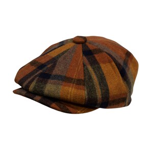 May include: A brown and orange plaid newsboy cap. The cap features a classic eight-panel design with a button on top and a small, stiff brim. The plaid pattern includes shades of brown, orange, yellow, and navy blue.