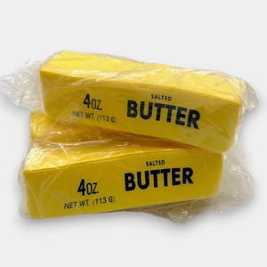 May include: Two yellow butter sticks, each wrapped in clear plastic. The butter is labeled "SALTED BUTTER" and "4oz NET WT. (113 G)". The image shows a close-up of the butter packaging.