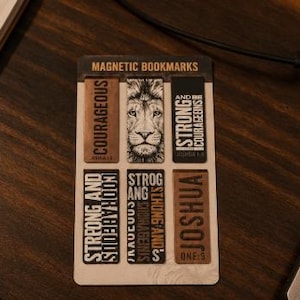 Pode incluir: Um conjunto de marcadores magnéticos com o rosto de um leão e palavras inspiradoras. Os marcadores são castanhos e pretos com textos como "Courageous", "Strong" e "Joshua". Apresentados numa superfície de madeira.