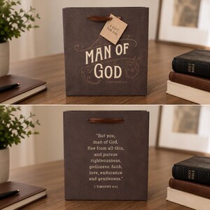 May include: A brown gift bag with the text "MAN OF GOD" in white script. A small tag reads "A GIFT FOR YOU". The bag has a brown handle and is on a wooden surface. A Bible and a journal are also visible.