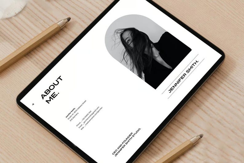 May include: A digital tablet displays a minimalist design with the text "ABOUT ME." and a black and white photo of a person. The name "JENNIFER SMITH" is also visible. Two pencils are on the wooden surface.