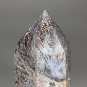 May include: A large, gray, white, and brown agate crystal point with a pointed top and a hexagonal base.