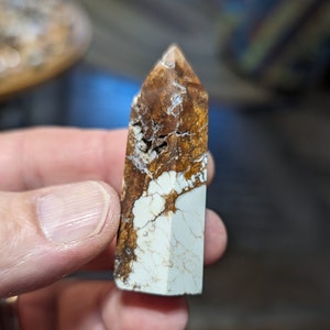 May include: A white and brown crystal point with a rough, natural texture. The crystal is pointed at the top and has a flat base.