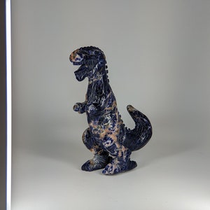 May include: A blue and white dinosaur figurine carved from lapis lazuli stone. The dinosaur is standing on a white surface.
