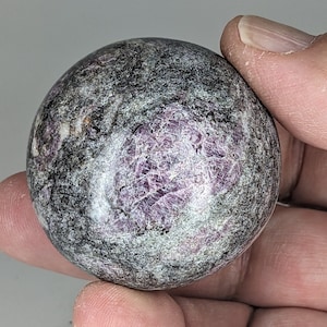 May include: A polished sphere of purple and grey gemstone with a swirling pattern. The sphere is about the size of a golf ball.