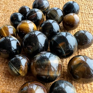 May include: A collection of tiger's eye spheres in various shades of brown, gold, and black. The spheres are smooth and polished, with a reflective surface.