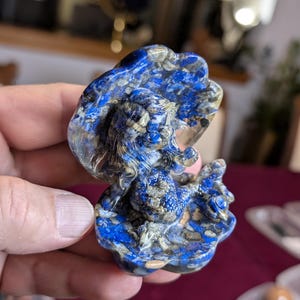 May include: A small, blue and white carved mermaid figurine made of lapis lazuli. The mermaid is sitting on a shell and has long flowing hair.