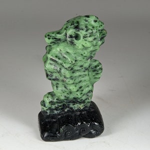 May include: A green and black jade carving of a seahorse standing on a black base. The seahorse is detailed with a textured surface.