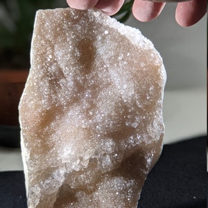 May include: A large, irregularly shaped, light brown geode with a cluster of small, clear quartz crystals on the surface.