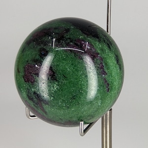 May include: A green and purple gemstone sphere on a metal stand. The sphere is polished and has a smooth surface.