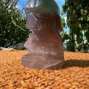 May include: A green and pink carved figurine of Darth Vader, a character from the Star Wars franchise. The figurine is made of a translucent material, possibly fluorite or selenite.