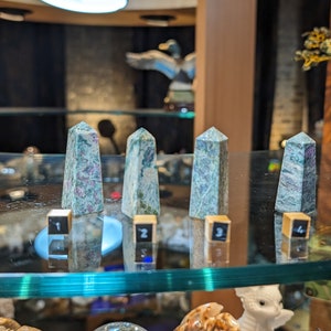 May include: Four green and pink crystal towers on a glass shelf with numbers 1 through 4 on small wooden blocks in front of each tower.