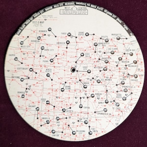 May include: A white circular map with red lines and black dots showing distances between cities in the central United States. The map is titled "West Central Dist-O-Map".