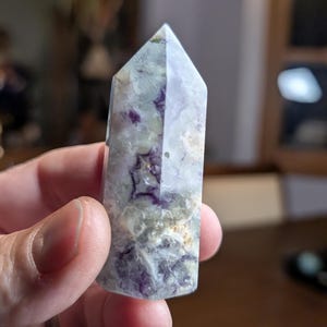 May include: A green and purple fluorite crystal point with a pointed tip and a flat base. The crystal has a natural, rough texture and is translucent.