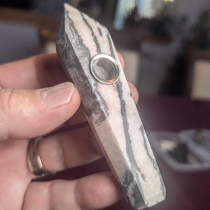 May include: A white and black striped stone pipe with a metal bowl. The pipe is held in a hand.