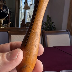 May include: A wooden, brown, and orange, smooth, rounded, tapered,  handle with a thin, vertical, dark brown line down the center.