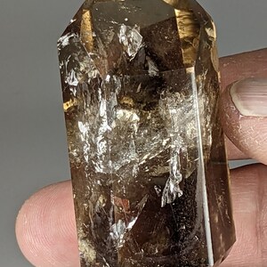 May include: A clear, faceted, smoky quartz crystal point with a golden hue. The crystal is approximately 2 inches tall and has a natural, rough texture.