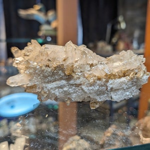 May include: A cluster of clear quartz crystals with a brown, earthy base. The crystals are arranged in a random, natural formation.