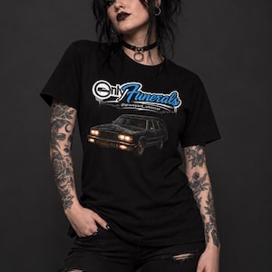 May include: A black short-sleeve t-shirt featuring a graphic of a hearse with the text Only Funerals in white and blue lettering above the vehicle and the social media handle @graveyard_whorror printed in smaller white text below the car.