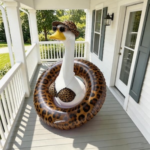 May include: A whimsical white goose wearing a leopard print hat, sunglasses, and bikini, inside a leopard print inflatable ring. The goose is on a porch with white railings and a door.