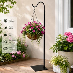 May include: A black metal hanging plant stand with a square base supports a hanging basket filled with vibrant pink flowers. The stand has a curved top and is designed for outdoor use. The image also shows a white window and other potted plants.